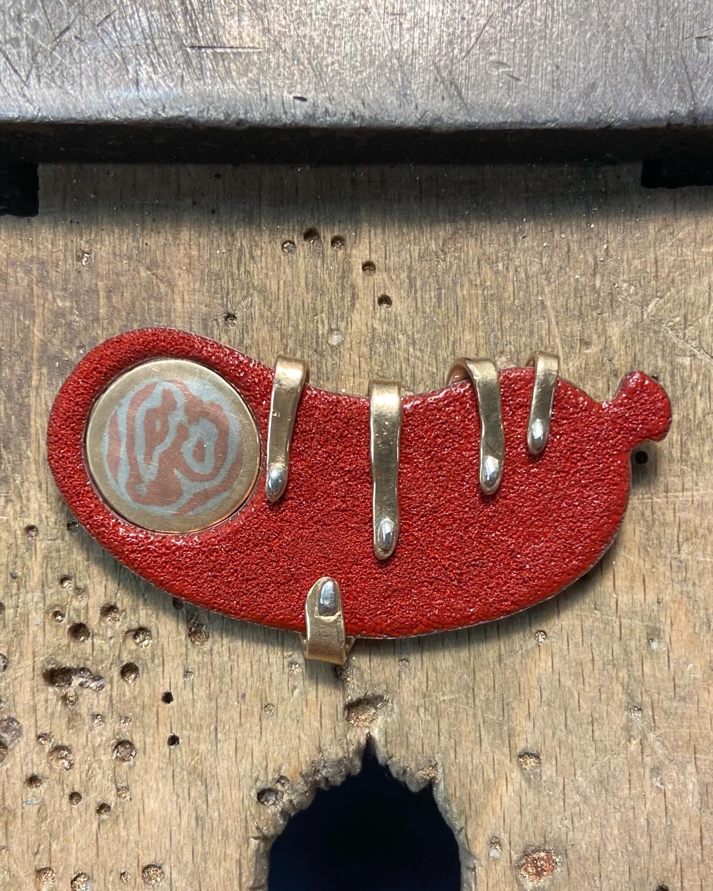 Mokume and enamel Sausage pin being held